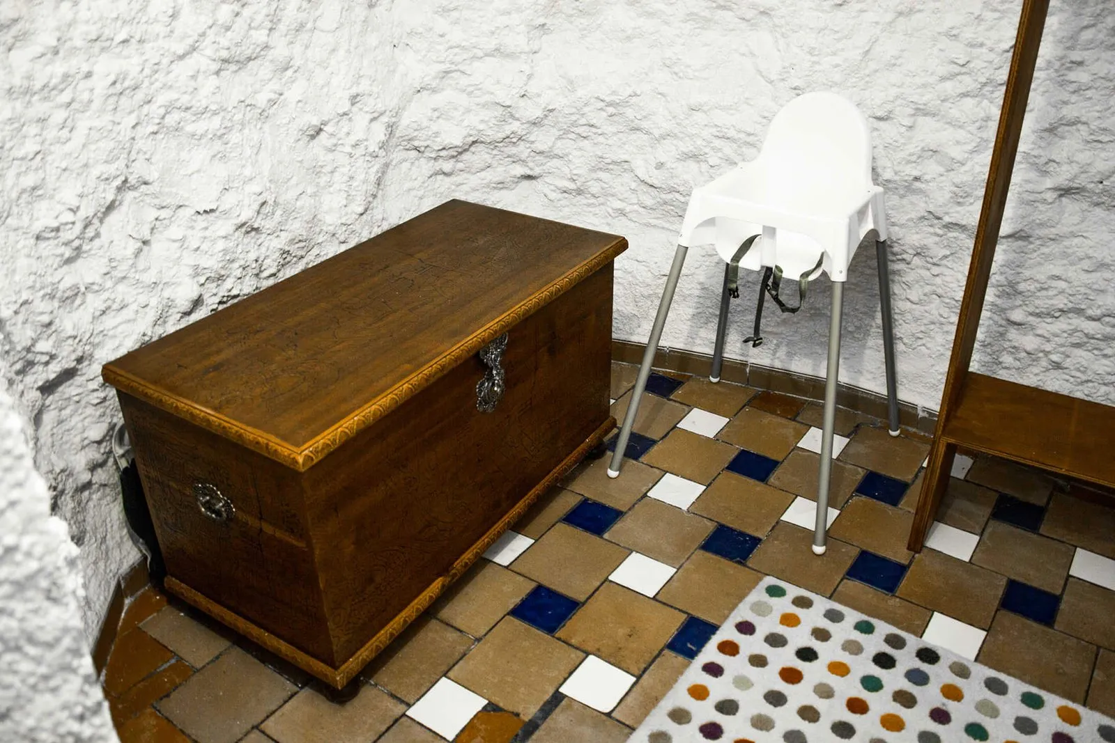 Dressing area with a wooden chest, high chair and colourful tiled floor